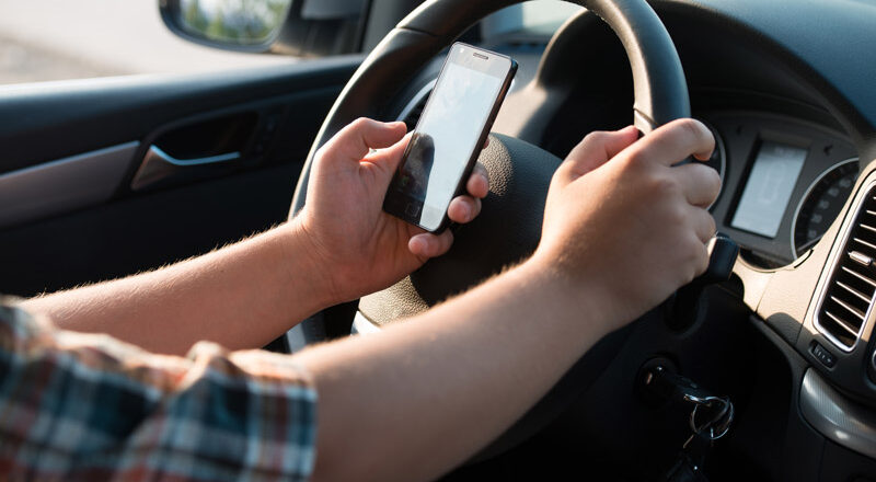 Texting and talking while driving, hands of young man on steering wheel